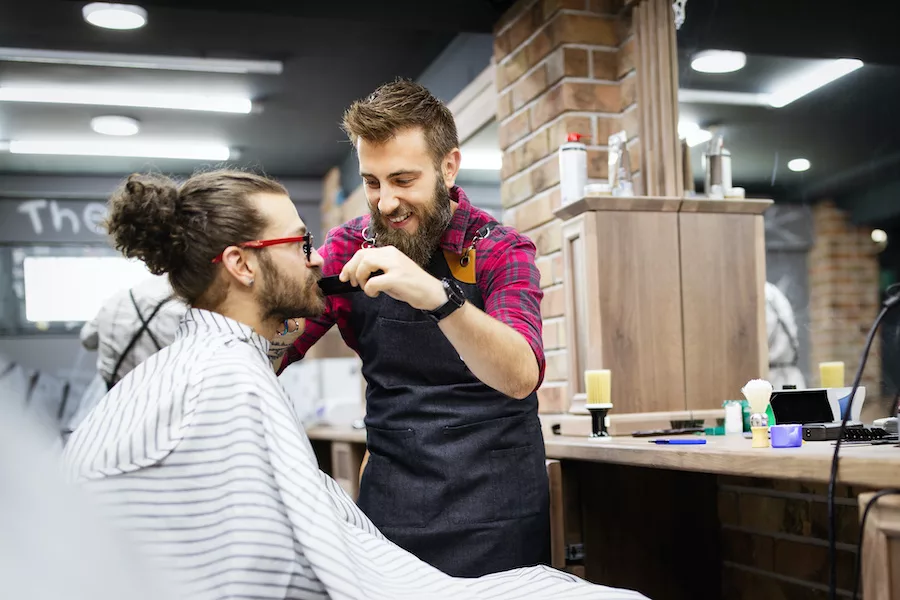 Happy young handsome man visiting hairstylist in barber shop salon